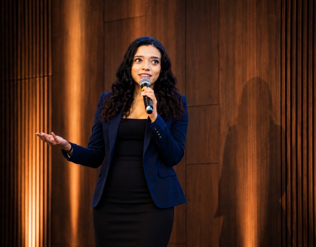 Alisha Outridge speaking with a microphone on a warmly lit stage